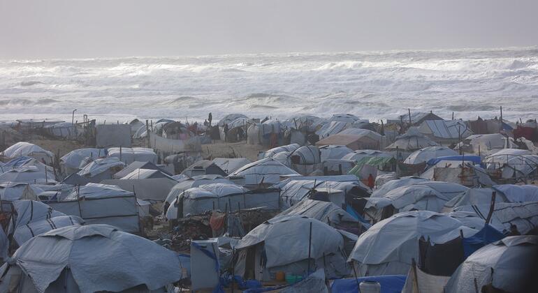 Un abarrotado campo de refugiados en Gaza con numerosas tiendas de campaña improvisadas a lo largo de la costa, con las olas rompiendo al fondo.